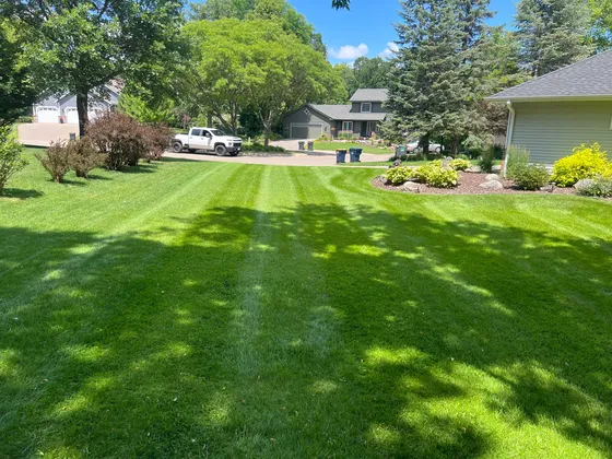 A freshly mowed residential lawn with clean mower stripes, an Ecosnow truck parked in the driveway beyond.