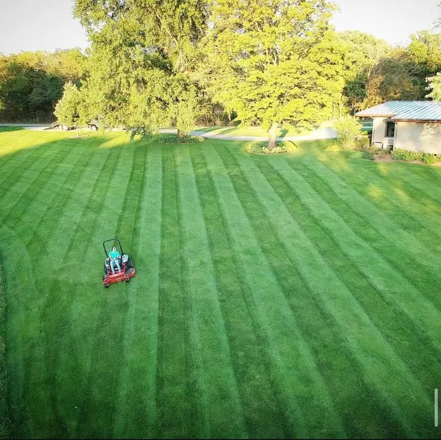 An Ecosnow zero-turn mower cutting clean stripes across a wide open lawn, seen from above.