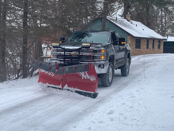 An Ecosnow pickup with a red V-plow pushing snow down a residential driveway after a storm.